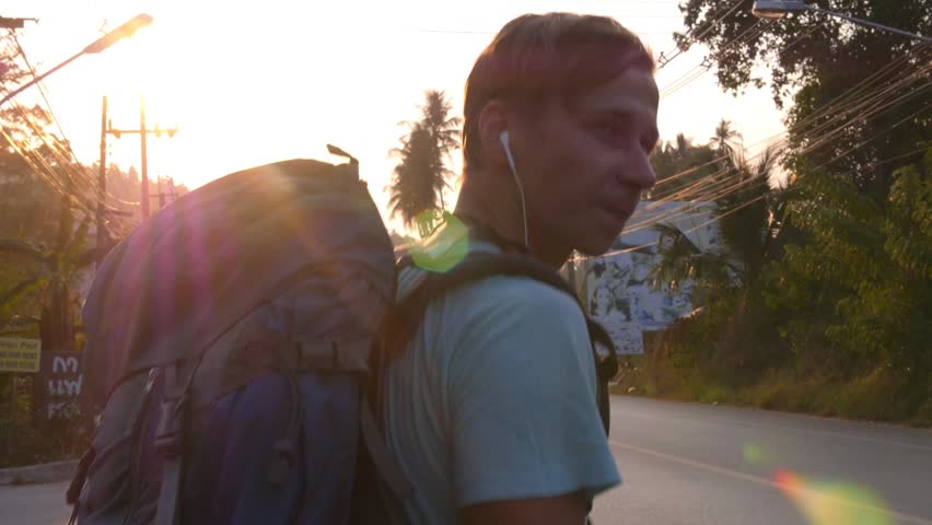Tourist with Backpack Hitchhiking on Road at Sunset in Travel