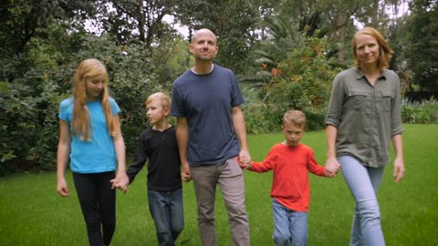 A smiling happy family of 5 look at and walk towards the camera - slowmo steadicam