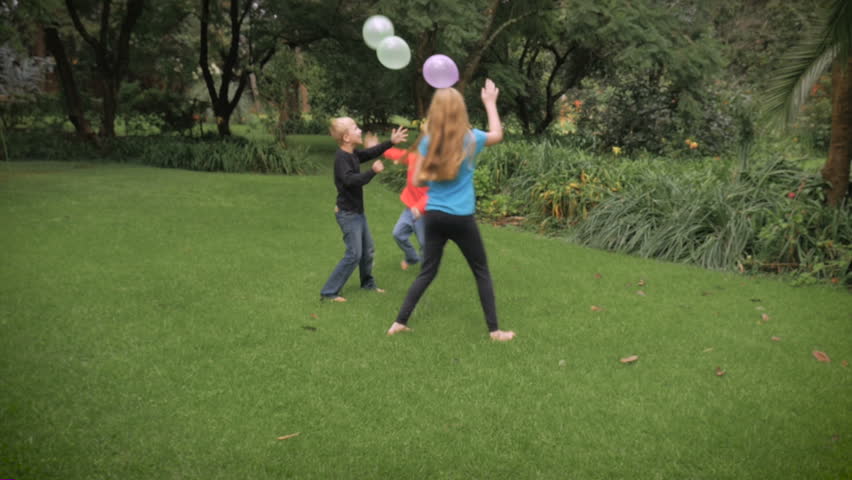 Three cute, young kids play together in a park with balloons in slowmo