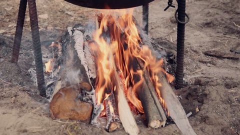 Campfire burning under a cauldron with blazing logs and hot coals in an outdoors cooking and catering concept