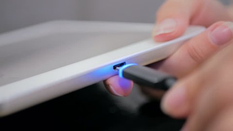 Woman's hand plugging black lightning charging cable into pc digital tablet - USB data cable connecting on modern gadget. Close up shot