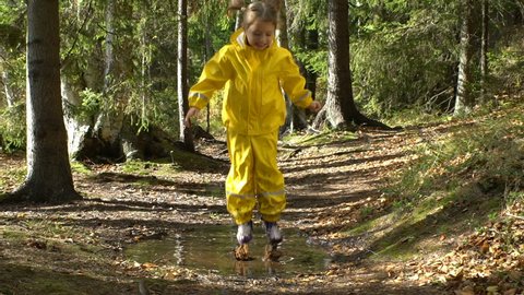 Little girl in a yellow rubber suit is jumping in a puddle. Slow motion.