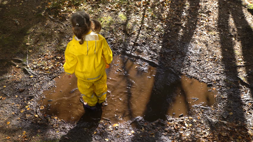 Little girl in a yellow rubber suit is jumping in a puddle.