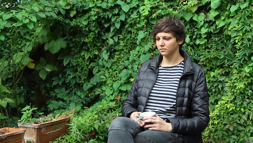 Young, happy woman drinking coffee  in the garden. In the background of green leaves