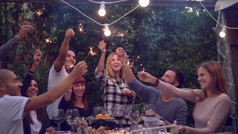Friends holding lit sparklers at a dinner party
