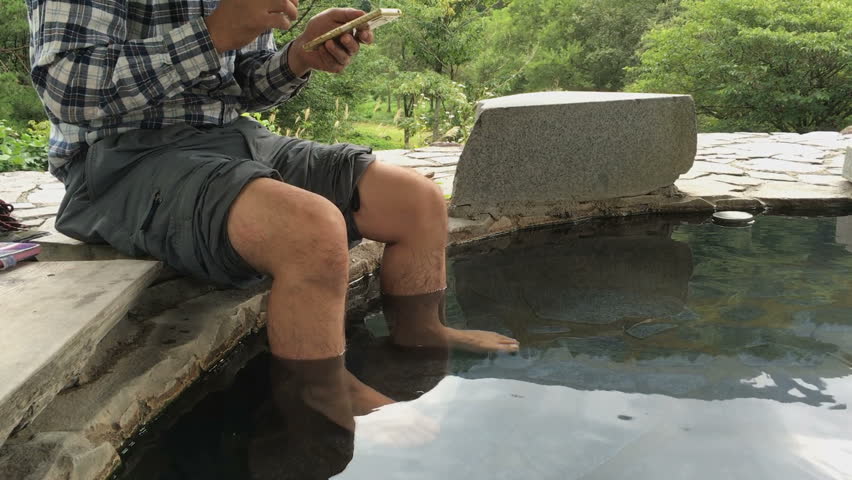 leg of man soaking feet at  hot springs and holding the phone. japanese  style