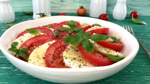 Delicious caprese salad with ripe tomatoes and mozzarella cheese with fresh basil leaves. Italian food. Slow motion.
