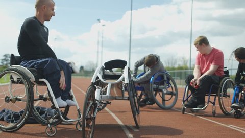 4K Disabled athletes prepare for training session at race track, 1 man climbs from his wheelchair into specially adapted racing chair. Shot on RED Epic.