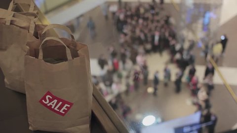 Man puts brown bags with sale sticker on it on floor in mall on black friday. Crowd on background