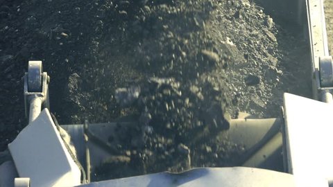 Cold milling machine, milled asphalt falls into the back of the truck, close up, top view, slow motion