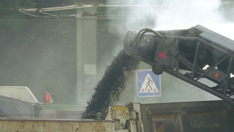 Removing the roadway cold mill, smoke above the conveyor belt with crushed asphalt, slow motion