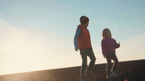 Boy and girl walking in front camera at sunset. Autumn landscape.
