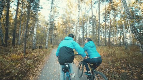 Lovers on biking in the autumn forest. Man and woman riding bicycles and holding hands. Romantic couple in a similar dress. Like-minded. Common interests. Together.