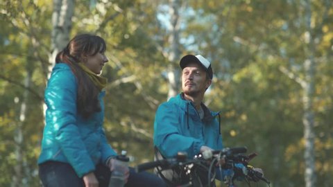 Young man and pretty young woman on a date in the autumn forest. Young and active man and woman. Boy and girl talking and laughing during a bike ride. Ease and laughter.