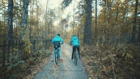Man and woman riding bikes on a beautiful country village. Couple going along the fence. Cycling on a clear day in autumn. Active lifestyle. Bike ride with a partner. Two bicycle.