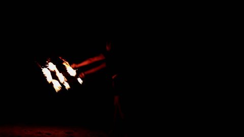 Girl dances with burning torches shaped as fans at fire show in evening.