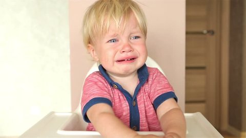 Little baby boy crying and sitting in his high chair.