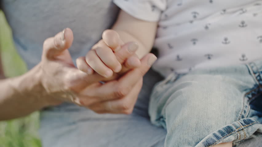 Close up with selective focus of little baby sitting on his mothers lap and holding her hand