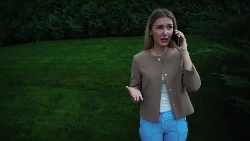 Communications, Showdown, Anger. Woman Girl Female Lady Blonde Long Hair Talking on Phone Angry, Indignant, Expresses Complaints Against the Background of Green Plant Landscaping. Royalty-Free Stock Footage #20300797