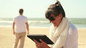 Happy young couple chatting on tablet computer on the beach