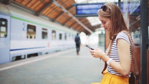 Young Woman Using Smartphone at Train Station. 4K. Girl texting on a Smart Phone while waiting for a train. Technology in everyday life and travel.