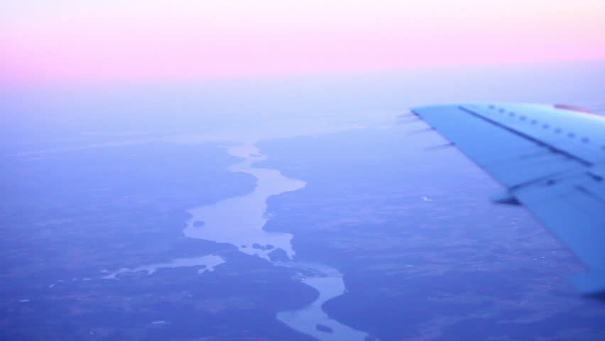 Aerial shot of airplane wing, land and sunset.