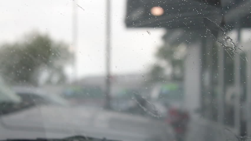 Inside of a car watching rain fall and wipers work.