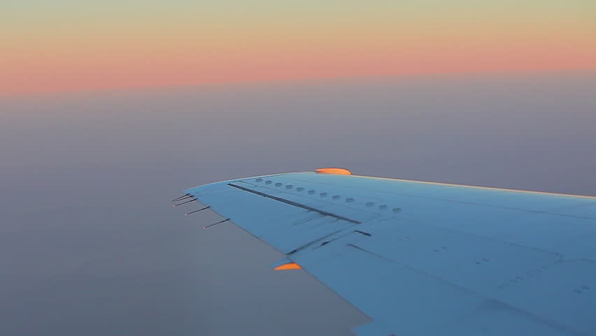 Airplane wing and the horizon with pink and yellow sky.