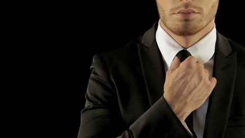 Caucasian male model in stylish black suite corrects his necktie. 