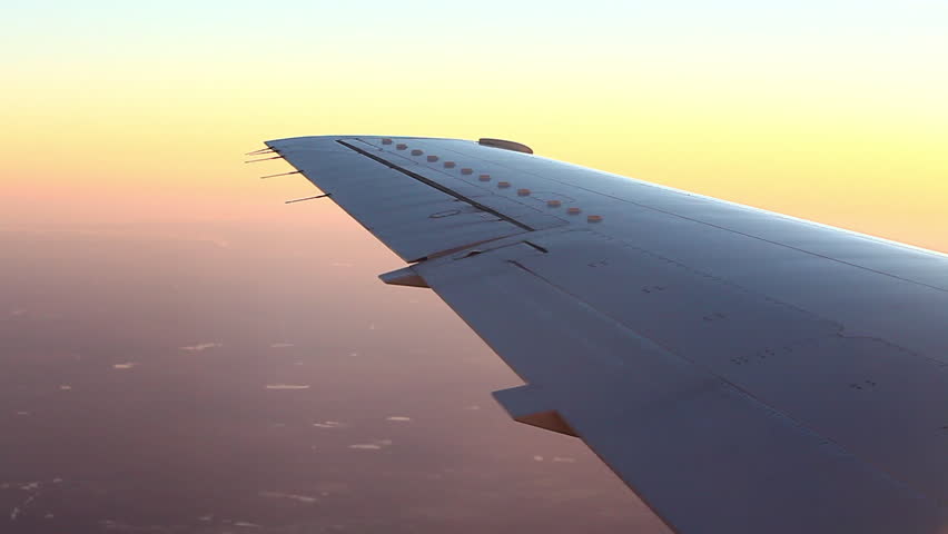 Airplane wing flying with pink and yellow horizon in distance.