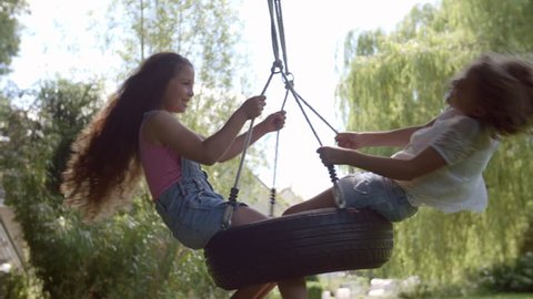 Two Girls Playing On Tire Swing In Garden