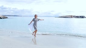 Beautiful graceful senior woman playful on sunny destination beach on holiday, outdoors. Senior healthy lifestyle fun, nature exterior. Wellness, well being energetic female with floating silk fabric.