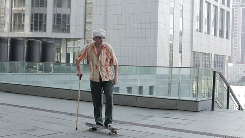 Old man with a cane riding on a skateboard.