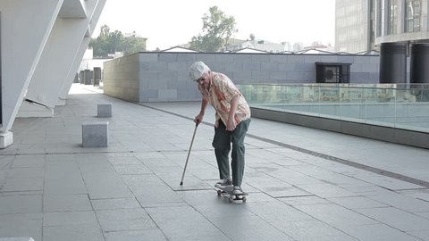Old man with a walking stick falls from the skateboard.