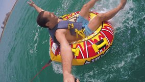 Man sitting in inflatable ring towed by a boat in the water and recording himself with Go Pro camera. He making faces to the camera.