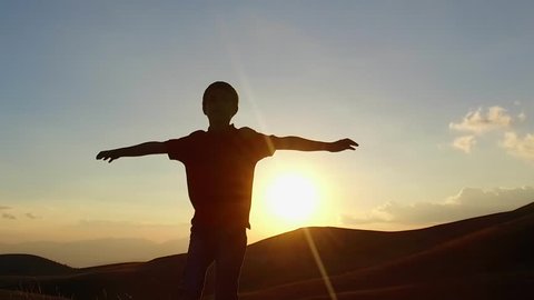 SLOW MOTION: Kid silouette spreading arms and looking to the infinite at the sunset. Conceptual footage. 