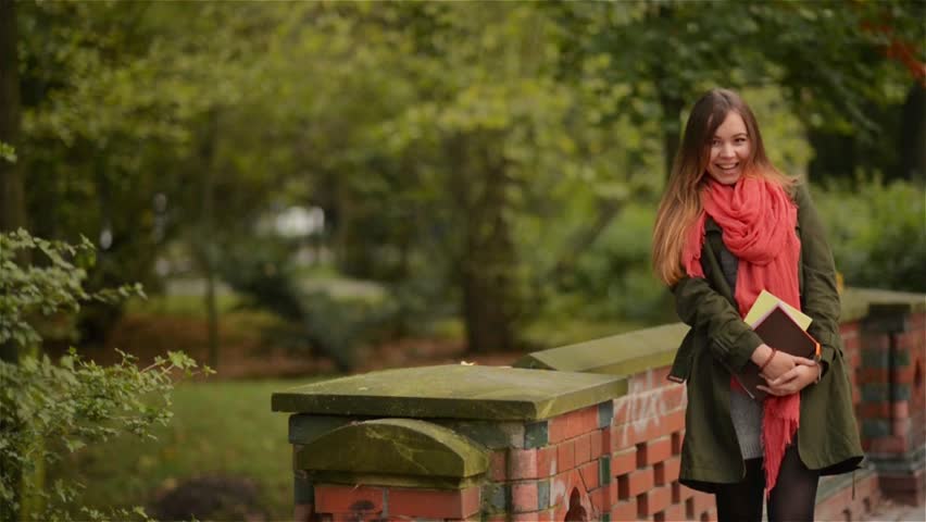 Student girl holding books wearing backpack outdoor smiling happy walking in the park. Caucasian female college or university student
