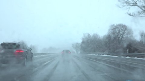 POV, CLOSE UP: Cars speeding on dangerous multilane highway with poor visibility on dark foggy winter day in severe snow blizzard. Wet snow falling on frosty road making driving conditions unbearable