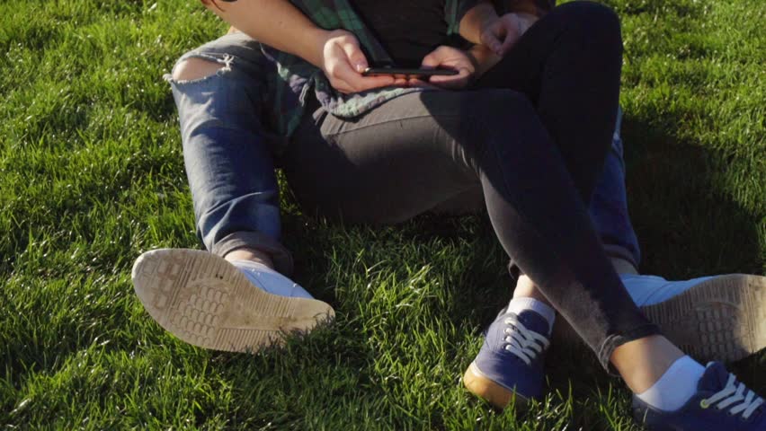 A couple lying on the grass watching photos at smartphone