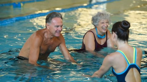 Happy smiling mature man and old woman cycling on a swimming bike. Happy and healthy senior people doing water aerobics on exercise bikes in a swimming pool. Fitness class training in swimming pool.