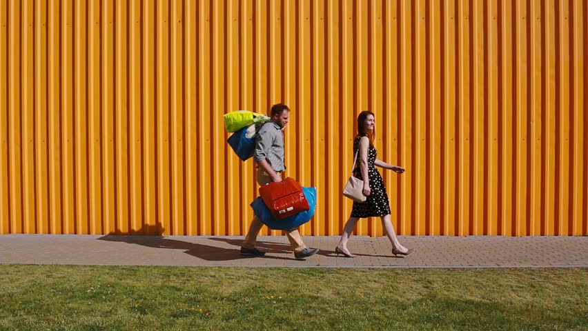 Young beautiful woman walking happily after shopping. Young men follows her struggling to carry her bags. Royalty-Free Stock Footage #20371069
