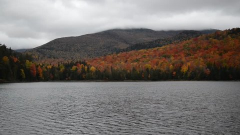 Vibrant Autumn foliage with red, orange and yellow fall colors in A Northeast forest with lake and clouds