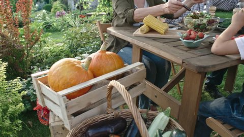 High angle tilt up of grandparents and grandchildren sitting behind patio table and enjoying organic harvest of vegetables and fruit
