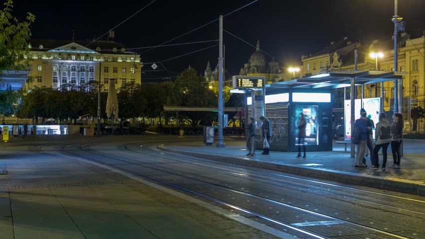 New modern trams of Croatian capital Zagreb night timelapse near railway station. People at tram stop at sunset time. ZAGREB, CROATIA