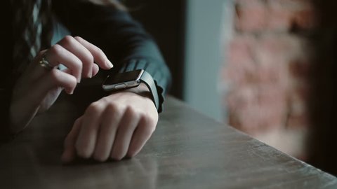 Hands closeup. Woman using her smartwatch touchscreen device in loft cafe 4k