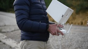 A bearded man dressed in the down jacket watching his tablet and smiling while piloting the drone in the fields, selective focus