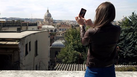 Young woman taking photo with of cityscape with cellphone in Rome, Italy
