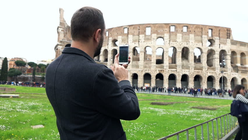 Young man taking photo of Colosseum with cellphone in Rome, Italy
