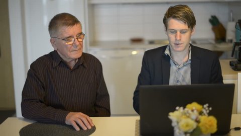 Senior man is watching while younger businessman is teaching how to use laptop computer