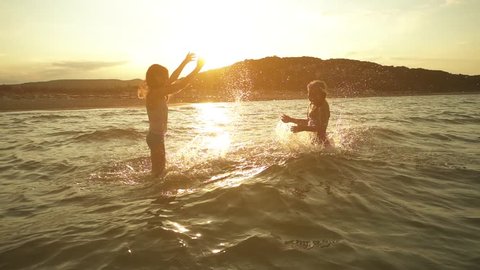 Slow Motion: Two little sisters splash water in the Baltic Sea on one another on the shores of Jurmala, Latvia.